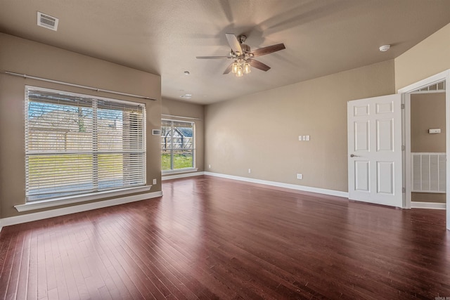 unfurnished room with visible vents, a ceiling fan, dark wood-type flooring, and baseboards