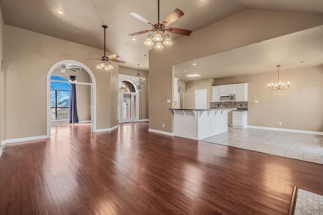 unfurnished living room featuring ceiling fan with notable chandelier, light wood-style floors, baseboards, and high vaulted ceiling