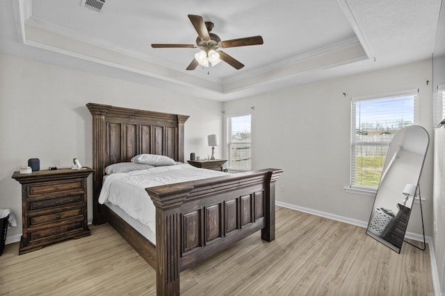 bedroom with a tray ceiling, crown molding, baseboards, and light wood-type flooring