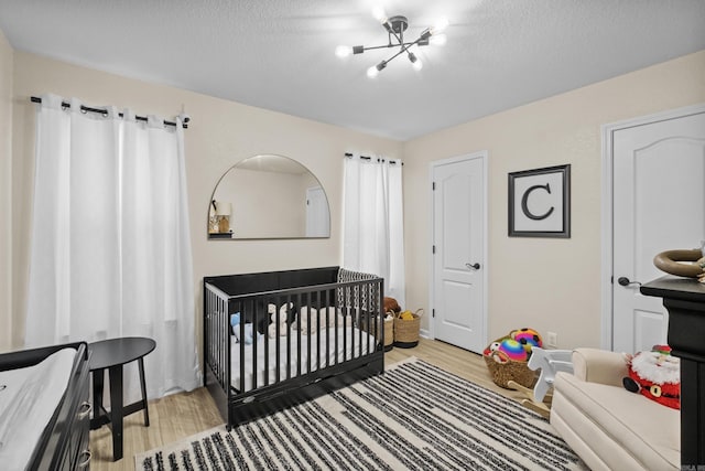 bedroom with light wood-style flooring, a textured ceiling, a crib, and an inviting chandelier