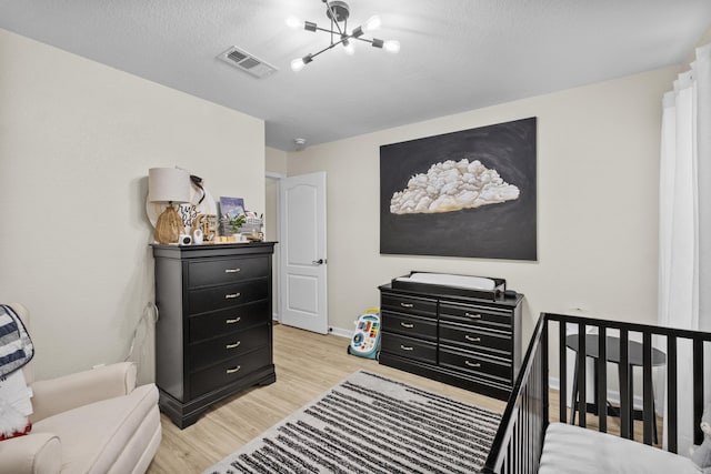 bedroom with visible vents, baseboards, light wood-style floors, a textured ceiling, and a chandelier