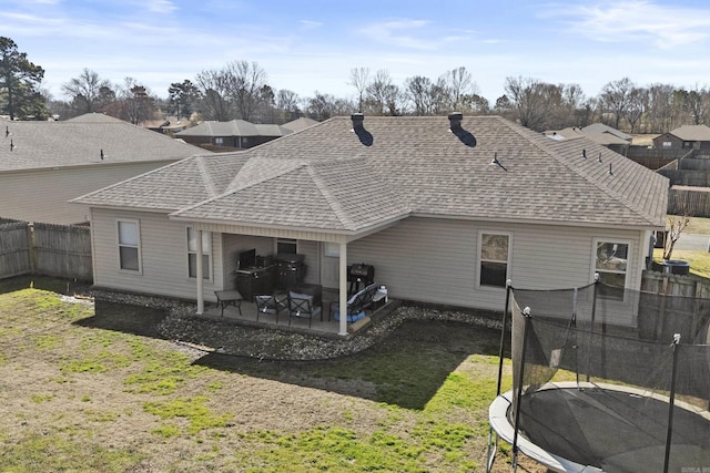 back of house featuring a patio, a trampoline, a fenced backyard, a yard, and roof with shingles