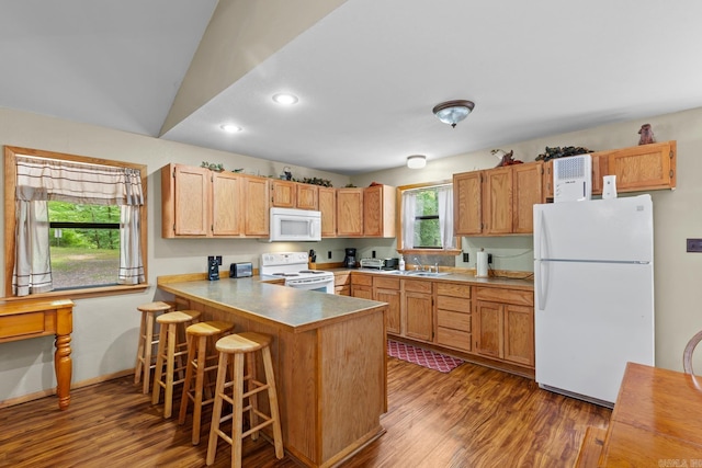 kitchen with a kitchen bar, white appliances, wood finished floors, and a peninsula