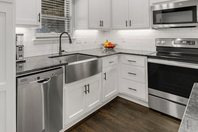 kitchen featuring dark wood finished floors, dark stone counters, a sink, stainless steel appliances, and backsplash