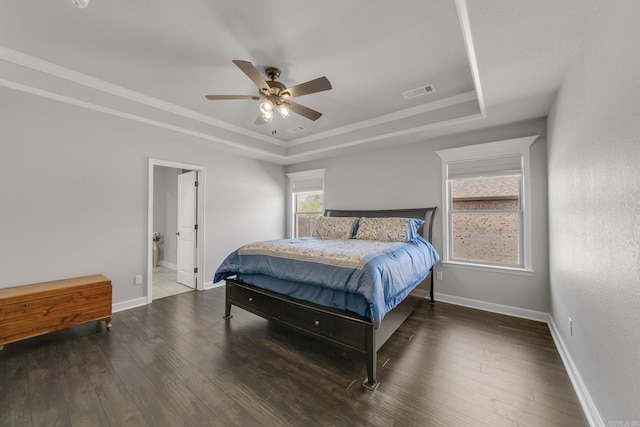 bedroom featuring a tray ceiling, baseboards, visible vents, and wood finished floors