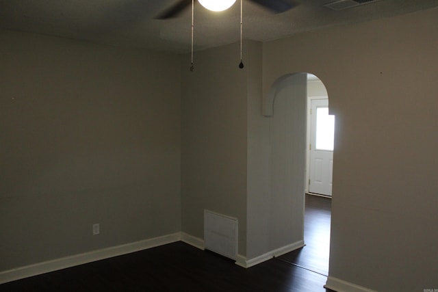 unfurnished room featuring visible vents, dark wood finished floors, arched walkways, baseboards, and ceiling fan