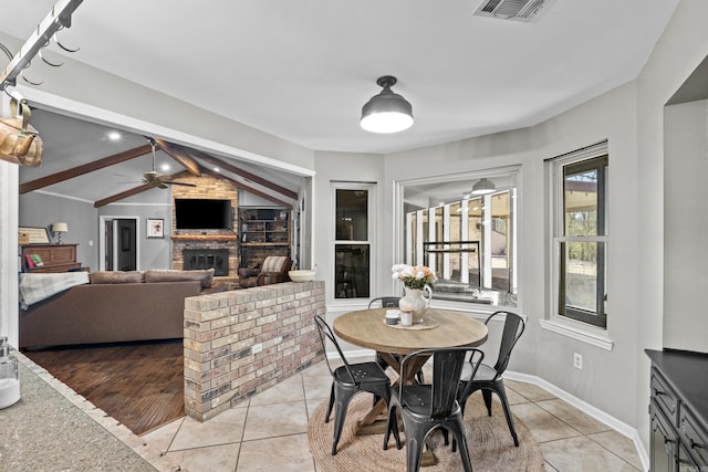 dining room with lofted ceiling with beams, light tile patterned flooring, a fireplace, and visible vents