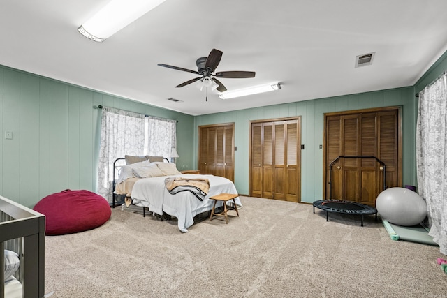 carpeted bedroom with visible vents, multiple closets, and a ceiling fan