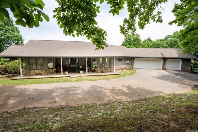 view of front of house with an attached garage, roof with shingles, covered porch, stone siding, and driveway