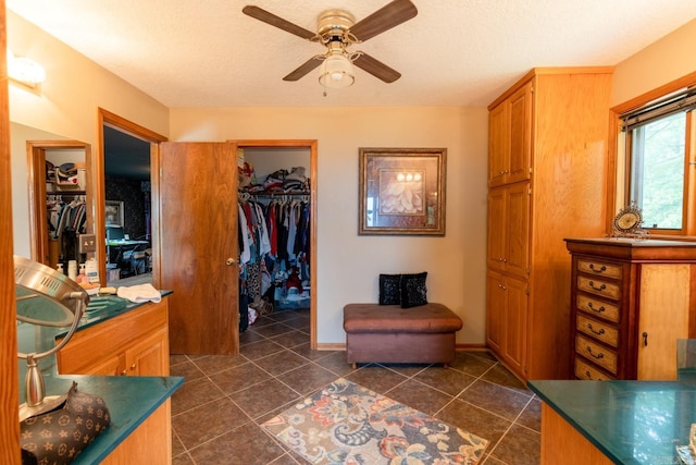 interior space featuring dark tile patterned floors, baseboards, a textured ceiling, and ceiling fan