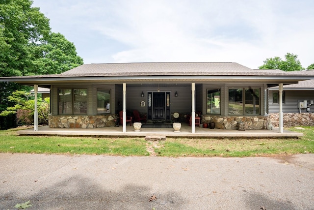 rear view of property featuring stone siding, covered porch, and roof with shingles