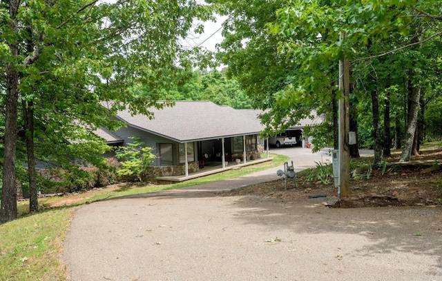 view of front of property with aphalt driveway, stone siding, a carport, and roof with shingles