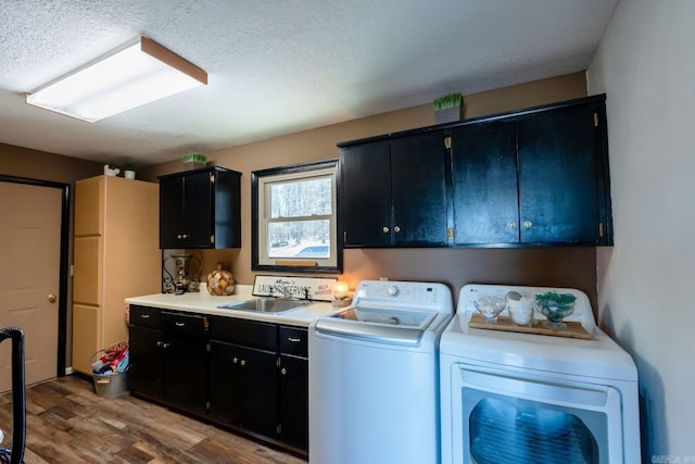 clothes washing area with washer and clothes dryer, a sink, a textured ceiling, wood finished floors, and cabinet space