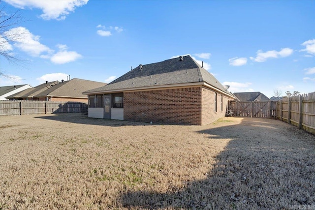 rear view of house with brick siding, a fenced backyard, a lawn, and a sunroom