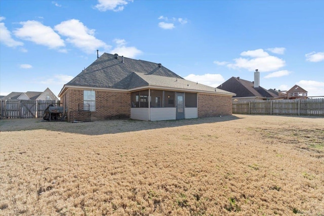 rear view of property featuring brick siding, a fenced backyard, a lawn, and a sunroom