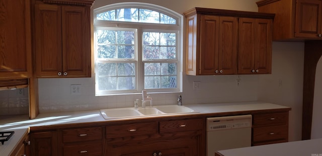 kitchen featuring a sink, tasteful backsplash, brown cabinetry, white dishwasher, and light countertops