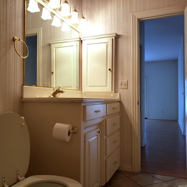 half bath featuring tile patterned floors, toilet, an inviting chandelier, wallpapered walls, and vanity