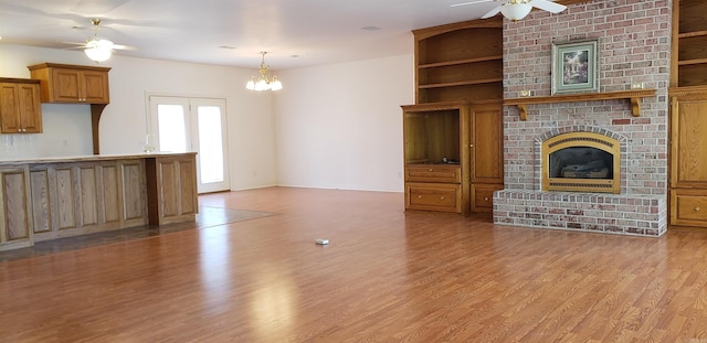 unfurnished living room with ceiling fan with notable chandelier, a fireplace, light wood-type flooring, and baseboards