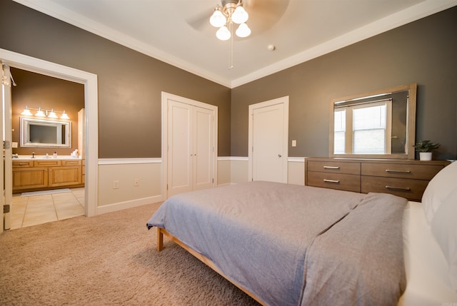 bedroom featuring light carpet, a ceiling fan, connected bathroom, a closet, and crown molding