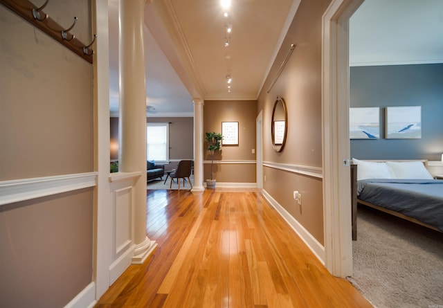 corridor featuring crown molding, decorative columns, baseboards, and light wood-type flooring