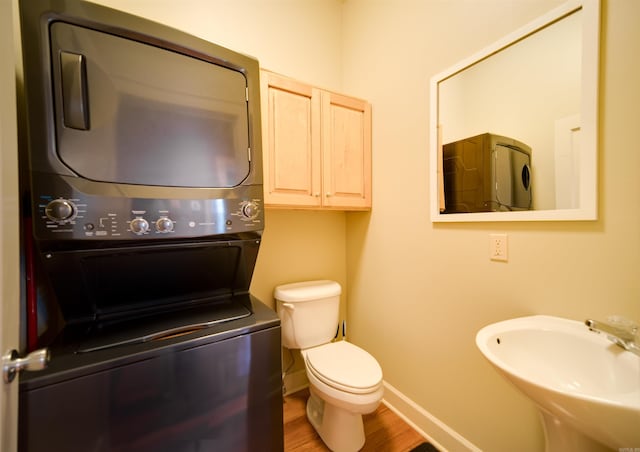 bathroom with baseboards, toilet, stacked washer and dryer, wood finished floors, and a sink