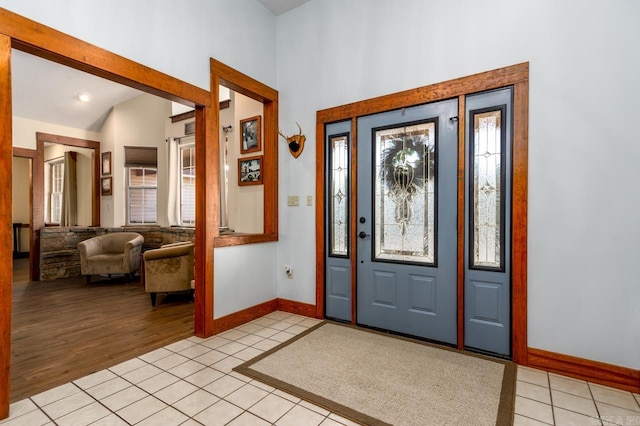 foyer entrance featuring lofted ceiling, light tile patterned flooring, and baseboards