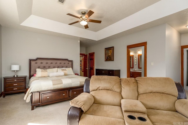 bedroom featuring visible vents, connected bathroom, a tray ceiling, light carpet, and a ceiling fan