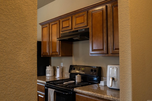 kitchen featuring electric range, a textured wall, and under cabinet range hood