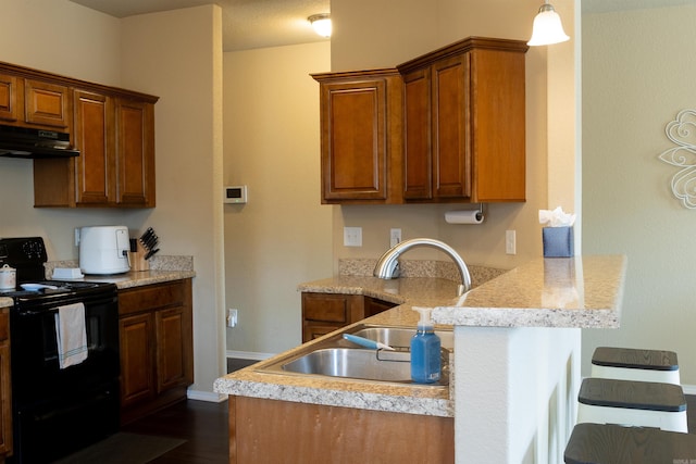 kitchen with black range with electric stovetop, under cabinet range hood, a peninsula, brown cabinetry, and a sink