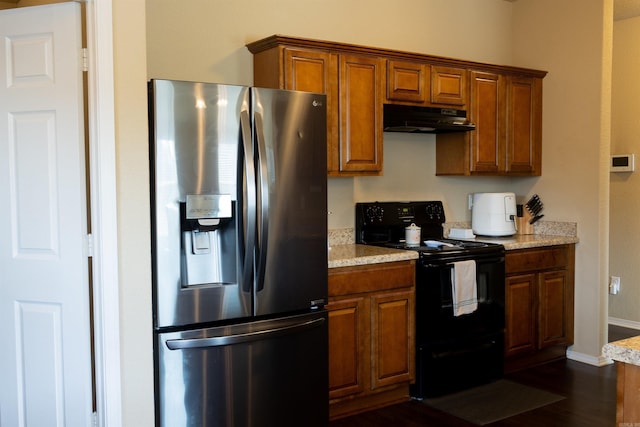 kitchen featuring under cabinet range hood, stainless steel fridge, brown cabinets, and black range with electric cooktop