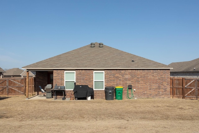 back of house with brick siding, a shingled roof, fence, a patio, and a gate