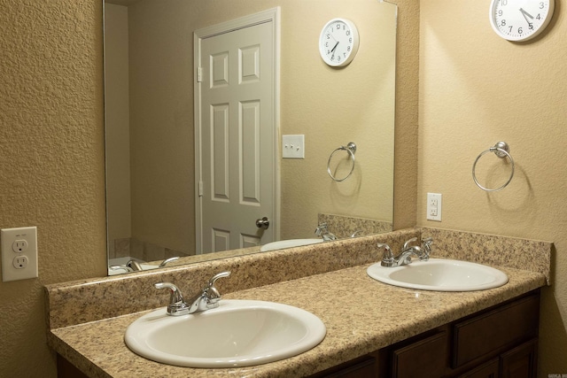 bathroom featuring double vanity, a textured wall, and a sink