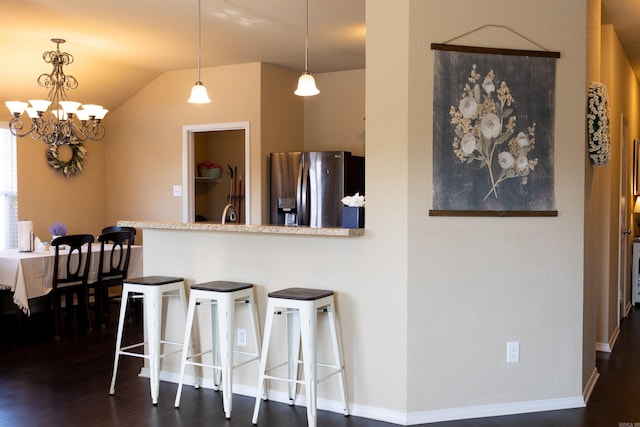 kitchen featuring a breakfast bar area, a peninsula, dark wood-style flooring, vaulted ceiling, and stainless steel fridge