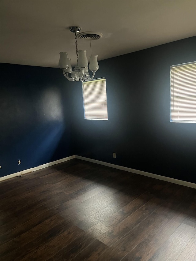 unfurnished room featuring a healthy amount of sunlight, dark wood finished floors, and a notable chandelier