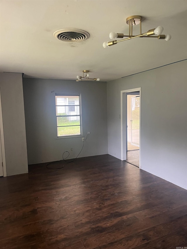 unfurnished room featuring visible vents, dark wood-style floors, and an inviting chandelier