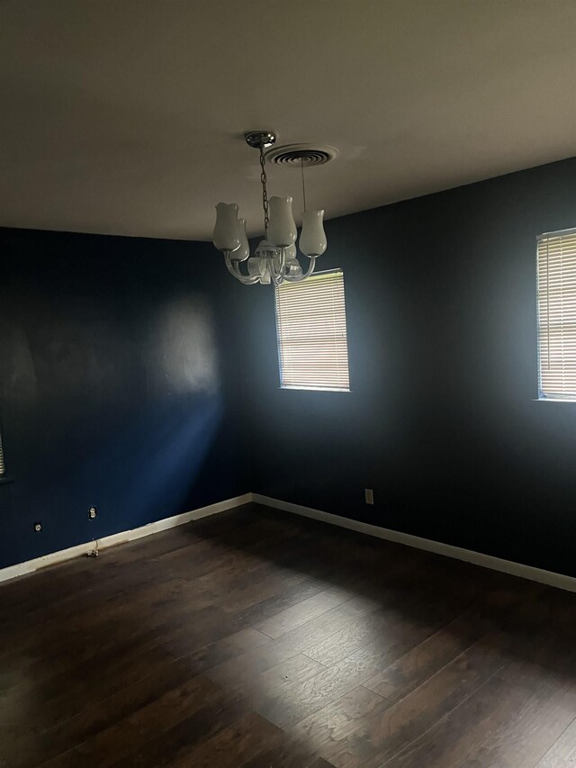 unfurnished room with baseboards, a chandelier, and dark wood-style floors