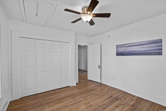 unfurnished bedroom with a ceiling fan, wood finished floors, a closet, baseboards, and attic access