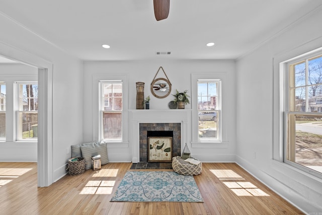 living area with a tiled fireplace, visible vents, a wealth of natural light, and wood finished floors