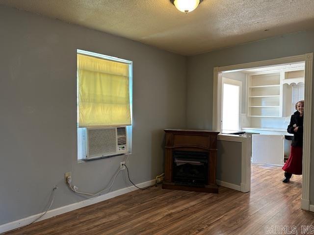 unfurnished living room with a textured ceiling, wood finished floors, cooling unit, a fireplace, and baseboards