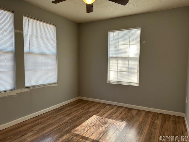 empty room featuring a ceiling fan, wood finished floors, baseboards, and a textured ceiling