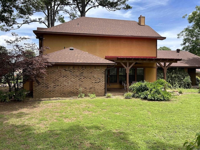 rear view of property with a yard, a shingled roof, a chimney, a patio area, and brick siding