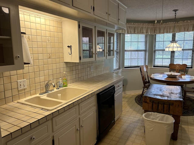 kitchen featuring glass insert cabinets, tile countertops, black dishwasher, a textured ceiling, and a sink