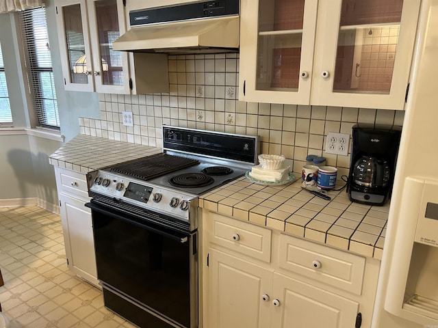 kitchen with under cabinet range hood, backsplash, stainless steel electric stove, white cabinets, and tile counters