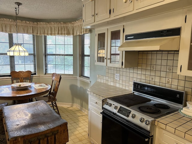 kitchen with tile countertops, electric range, under cabinet range hood, a textured ceiling, and white cabinetry