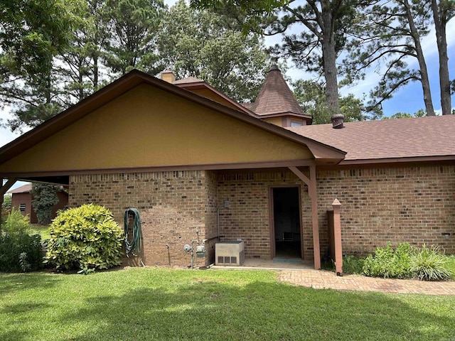 rear view of house with a yard, brick siding, and roof with shingles