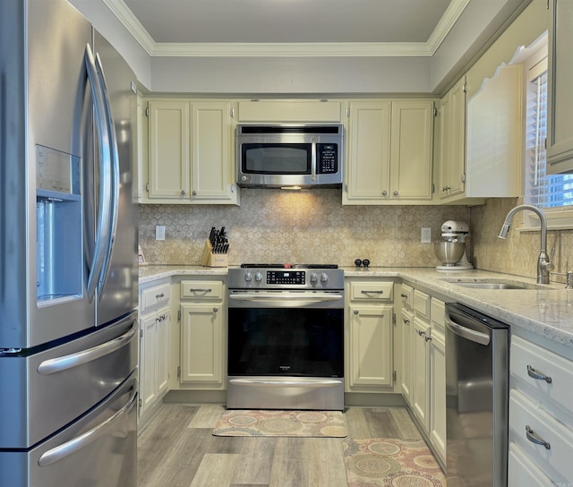 kitchen featuring light wood-style flooring, ornamental molding, a sink, appliances with stainless steel finishes, and decorative backsplash