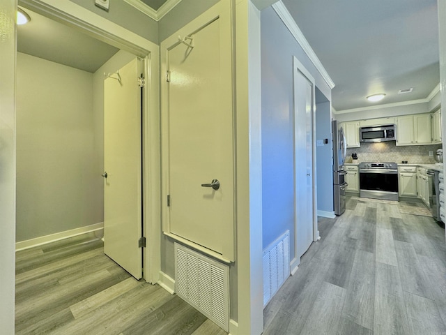 hall featuring visible vents, baseboards, crown molding, and light wood finished floors