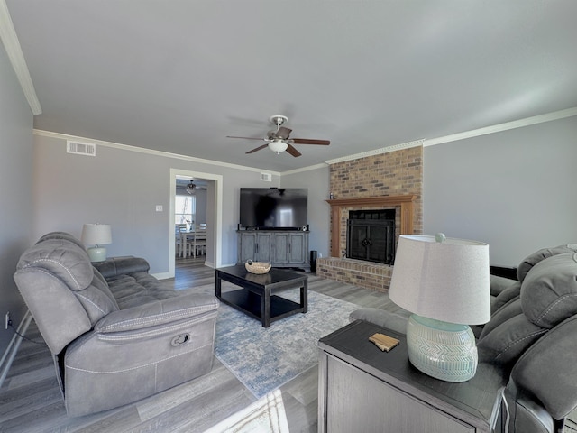 living room with light wood-type flooring, visible vents, a fireplace, and crown molding