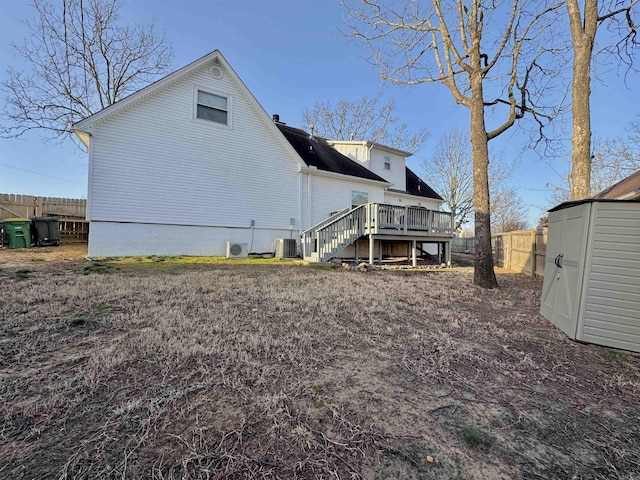 rear view of property featuring a wooden deck, stairs, a storage shed, a fenced backyard, and an outbuilding