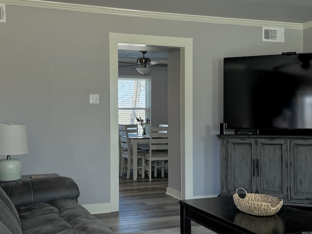 living area with visible vents, dark wood-type flooring, baseboards, ornamental molding, and a ceiling fan